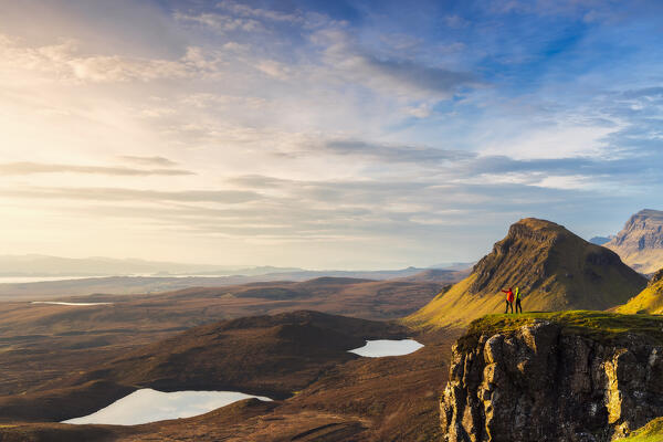 Two trekkers observe mountains from Quiraing viewpoint during sunrise, Isle of Skye, Inner Hebrides, Highlands, Scotland, United Kingdom