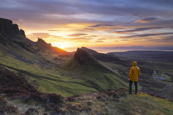 Tourist observes mountains and sunrise from Quiraing viewpoint during sunrise, Isle of Skye, Inner Hebrides, Highlands, Scotland, United Kingdom