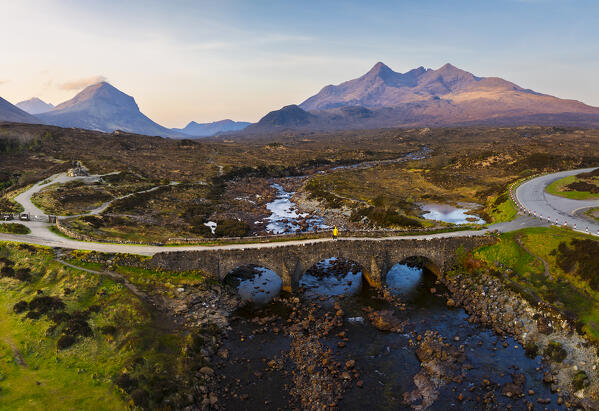 Aerial and panoramic view of a tourist on Sligachan Old Bridge observes Black Cuillin at sunrise, Isle of Skye, Inner Hebrides, Trotternish peninsula, Highlands, Scotland, United Kingdom (MR)