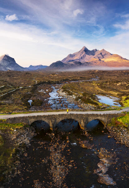 Aerial view of a tourist on Sligachan Old Bridge observes Black Cuillin at sunrise, Isle of Skye, Inner Hebrides, Trotternish peninsula, Highlands, Scotland, United Kingdom