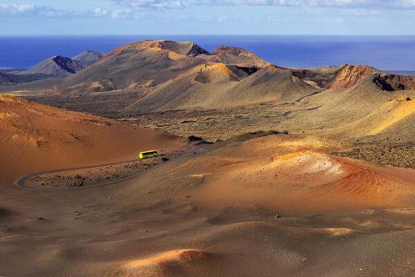 A bus travels through lava fields and volcanoes of Timanfaya National Park during sunrise, Yaiza, Las Palmas, Timanfaya National Park, Lanzarote, Canary Islands, Macaronesia, Spain, Western Europe
