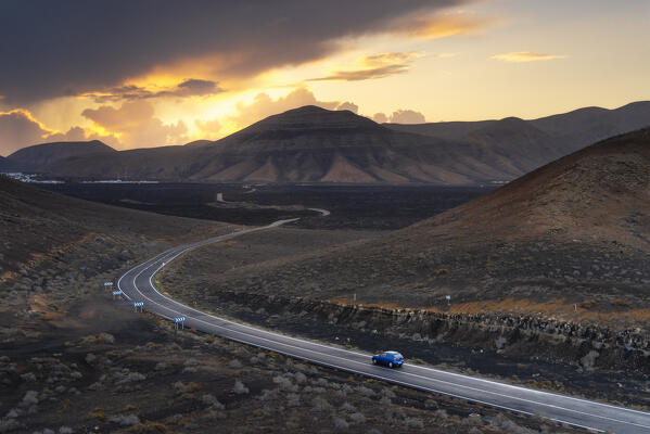 A car travels towards Yaiza surrounded by lava fields and volcanoes around Timanfaya National Park during sunrise, Yaiza, Las Palmas, Timanfaya National Park, Lanzarote, Canary Islands, Macaronesia, Spain, Western Europe