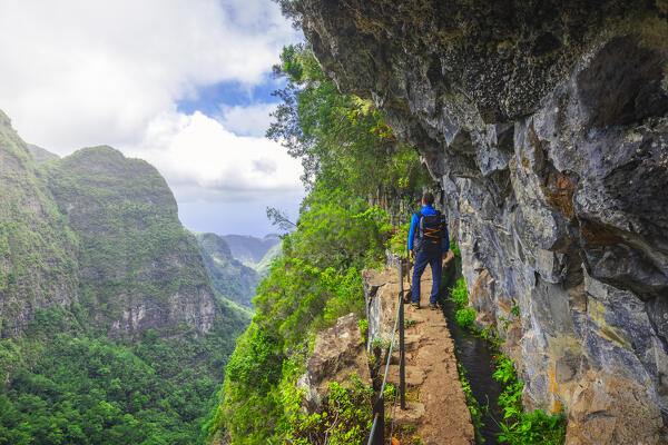 A tourist walks through beautiful and lush nature of Levada do Caldeirao Verde and the view of mountains and valley, Sao Vicente, Parque Florestal das Queimadas, Levada do Caldeirao Verde, Madeira region, Portugal, Western Europe