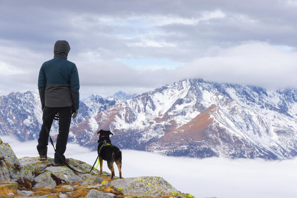 A man with his dog at Paradise Pass over Tonale Pass observes mountains and clouds in front of him, Ponte di Legno, Brescia, Lombardia, Italy, Southern Europe (MR)