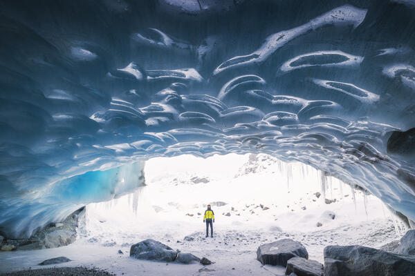 A trekker observes the entrance of an ice cave at Morteratsch glacier during winter, Bernina Valley, Grigioni, Switzerland, Western Europe