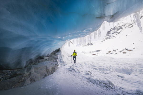 A trekker observes the entrance of an ice cave at Morteratsch glacier during winter, Bernina Valley, Grigioni, Switzerland, Western Europe