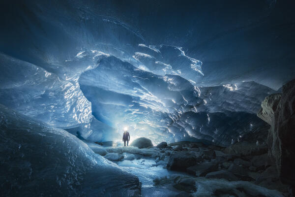 A trekker observes the entrance of an ice cave at Morteratsch glacier during winter, Bernina Valley, Grigioni, Switzerland, Western Europe