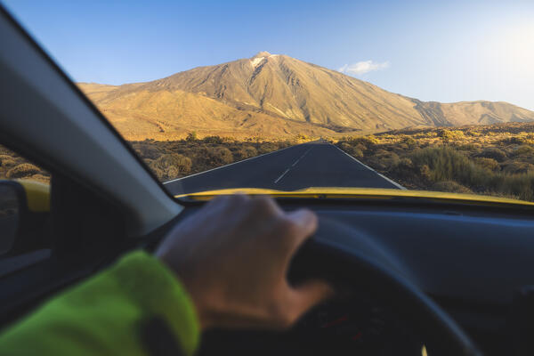 A tourist drives his car along the main road of Teide National Park in front of Teide volcano during sunrise, Teide National Park, La Orotava, Santa Cruz de Tenerife, Tenerife, Canary Islands, Macaronesia, Spain, Western Europe