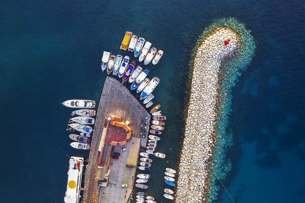 Aerial view of colourful boats and fishing vessels moored in the turquoise waters of the harbour of Ponza with the lighthouse and rocks at sunset, Ponza island, Archipelago Pontino, Latina province, Latium, Italy