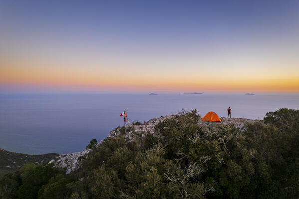 Hiker stands on top of Circeo peak near his tent enjoying the view of Pontine islands, Circeo National Park, Tyrrhenian sea, Mediterranean sea, Latina province, Latium, Central Italy, Italy, Southern Europe, Europe (MR)