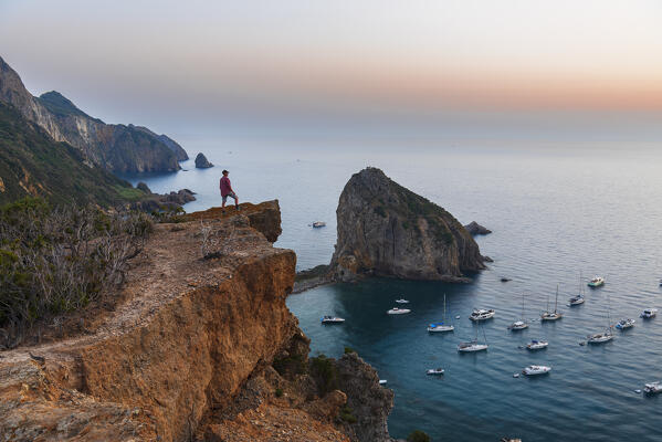 Man stands on top of the cliff above the bay of Palmarola with boats anchored at the sea, dusk time, Ponza municipality, Pontine archipelago, Latina province, Latium region, Tyrrhenian Sea, Italy, Europe (MR)