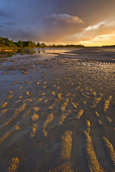 Po river park, Piedmont, Italy. Beach on Po river's banks, with clouds coloured by the sunset's lights.