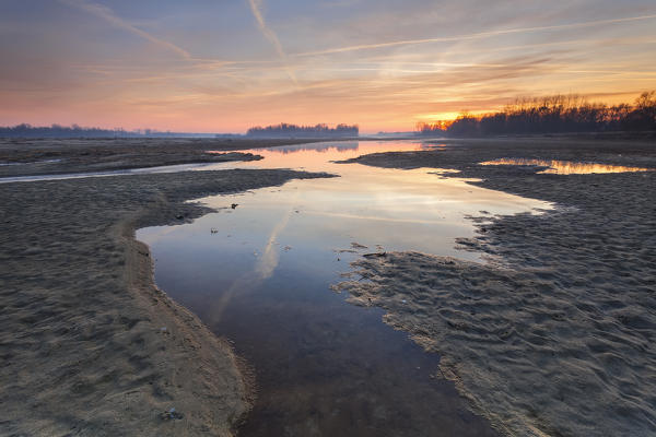 Po river park, Italy. Creeks in the sand with the reflection of a coloured winter sunset