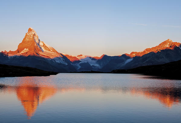 An alpine lake reflecting the Matterhorn and other peaks in the sunrise's colours. Valais, Swiss alps
