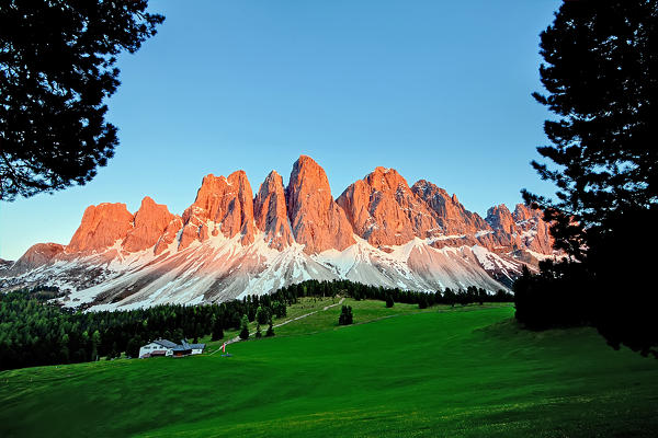 Lush green Meadows and a little cottage, under The Dolomite's peak, coloured by the sunset's lights, Italy
