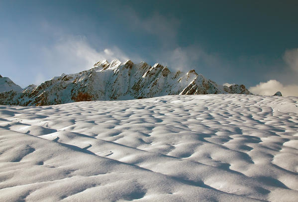 Snow surface and windswept mountain's ridge, in wintertime Valtellina, Lombardy, Italy
