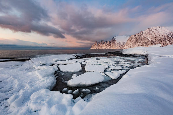 Ice blocks at the shore of jevelens tanngard in front of okshornan peaks (devil's jaw) at sunset, senja, nordland, norway, europe