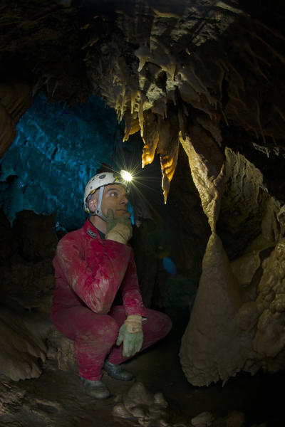 A spelunker in a cave watches the concretions on the wall with the light of his helmet