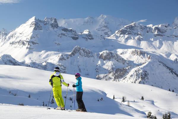 Skiers on ski slopes of Cherz framed by the high peaks of Marmolada and Portavescovo Arabba Dolomites Belluno Veneto Italy Europe
