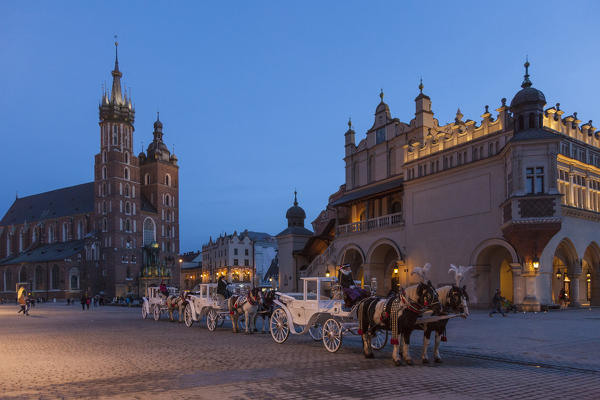 Rynek Glowny square, Krakow, Poland. St Mary basilica and carraiges with horses in the main market square, the biggest medieval square in Europe.