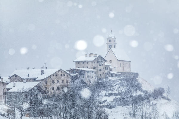 the ancient village of Colle Santa Lucia with the church on the hill under a snowfall, agordino, belluno, veneto, italy
