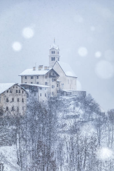 the ancient village of Colle Santa Lucia with the church on the hill under a snowfall, agordino, belluno, veneto, italy