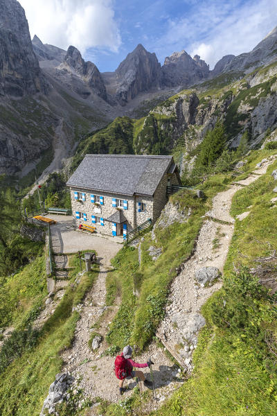 Hiker leaving the hut Onorio Falier at Pian di Ombretta, Ombretta valley, Marmolada, Dolomites, Belluno, Veneto, Italy