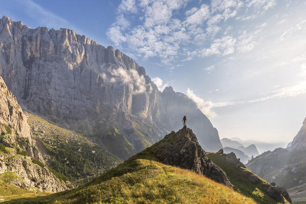 hiker standing on a hill facing the south wall of the Marmolada, in the Ombretta valley, Dolomites, Agordino, Rocca Pietore, Belluno, Veneto, Italy