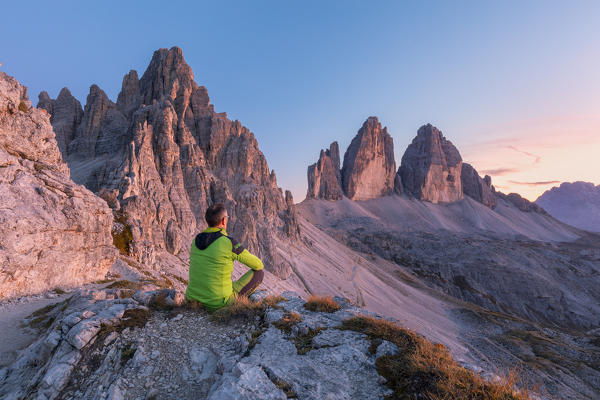 man sitting on the edge of the rocks admires the tre cime di lavaredo at sunset, Bolzano, South Tyrol, Italy, Europe