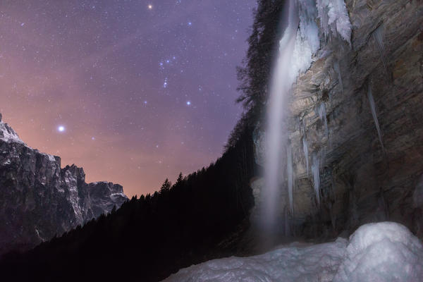The cascade of hell (Cascata dell'Inferno)at the end of the valley of San Lucano, Taibon Agordino. Photographed in the winter under a starry sky with the constellation of Orion. Dolomites, Belluno.