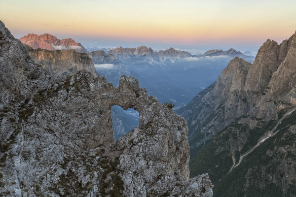 Sunset in front of the heart shaped arch of stone over the ridges of the Pale of the Balconies, Pala group, Dolomites. Europe, Italy, Veneto, Agordino.