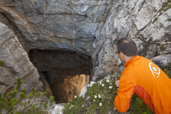 Europe, North Italy, Veneto, Belluno, Monti del Sole, Dolomites. Hiker leans over on the edge of the impressive Bus de le neole (hole of the clouds)