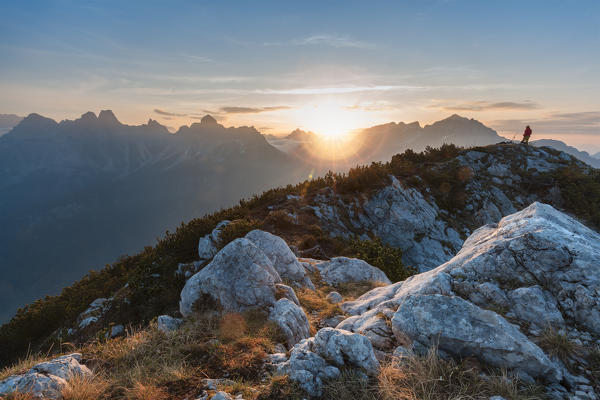 Europe, Italy, Veneto, Belluno. Hiker is looking at the rising sun fron the top of mount Celo, Dolomites, Agordino valley