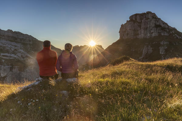 europe, Italy, Veneto, Agordino. Couple of trekkers sitting admiring the sunset near the bivouac Bedin at the First Pala di San Lucano, Dolomites.