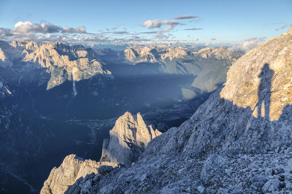 shadow of a mountaineer on the summit of Mount Agner, further down in the valley Taibon and Agordo already in the shadow, Agordino, Belluno, Veneto, Italy