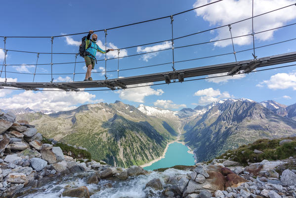 Hiker on the tibetan bridge near Olperer hut with Schlegeispeicher lake on the background, Zillertal Alps, Tyrol, Schwaz district, Austria.