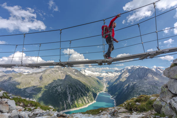 Hiker on the tibetan bridge near Olperer hut with Schlegeispeicher lake on the background, Zillertal Alps, Tyrol, Schwaz district, Austria (MR)