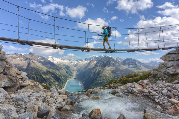 Hiker on the tibetan bridge near Olperer hut with Schlegeispeicher lake on the background, Zillertal Alps, Tyrol, Schwaz district, Austria.