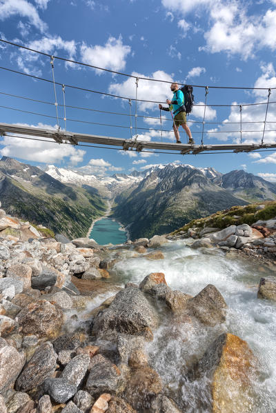Hiker on the tibetan bridge near Olperer hut with Schlegeispeicher lake on the background, Zillertal Alps, Tyrol, Schwaz district, Austria.