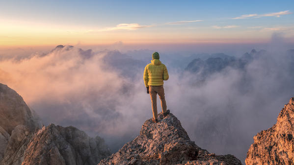mountaineer admires the landscape at sunrise from a rock spur near Punta Penia, Marmolada, Belluno and Trento, Dolomites, Italy (MR)