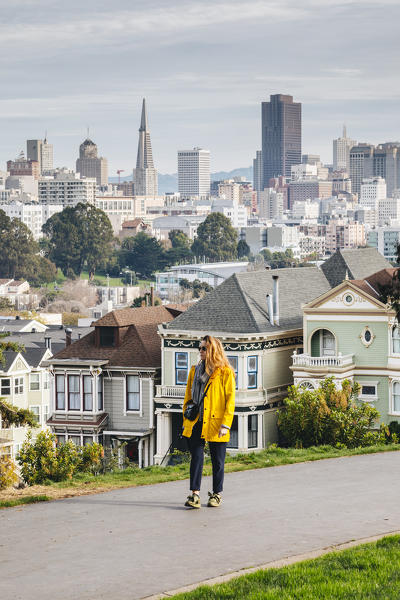 A girl walking in Alamo square, with financial district on the background, San Francisco, California, United States Of America