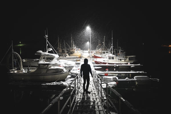 A man standing in front a Lofoten harbour during night while snowing. Lofoten  Islands, Nordland, Norway.