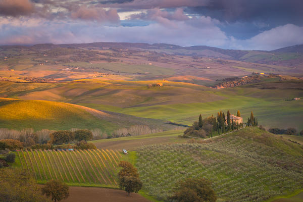 San Quirico d'Orcia, Tuscany, Italy. Sunset over the valley with some farmhouses and a very cloudy sky.