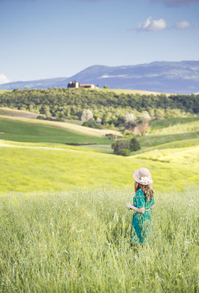 A girl in a green dress walking trough the golden fields of Tuscany. Val d'Orcia, Province of Siena, Tuscany, Italy