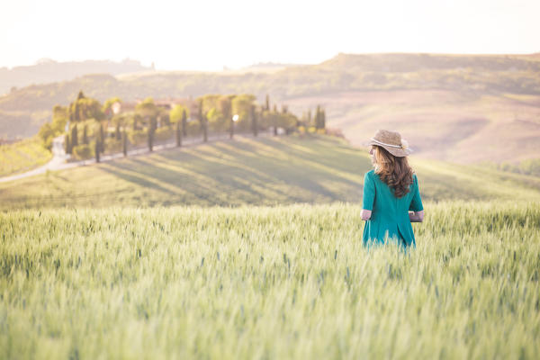 A girl in a green dress walking trough the golden fields of Tuscany. Val d'Orcia, Province of Siena, Tuscany, Italy