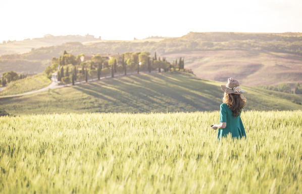 A girl in a green dress walking trough the golden fields of Tuscany. Val d'Orcia, Province of Siena, Tuscany, Italy