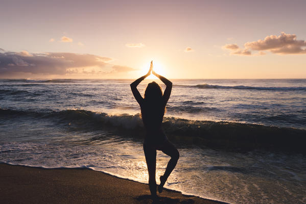 A girl doing yoga positions during sunrise in Kapaa beach park