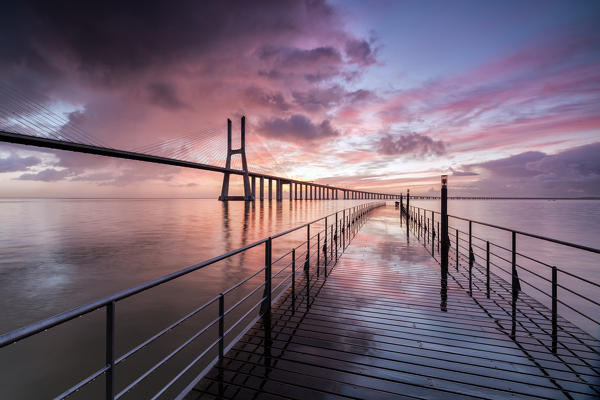 Sunrise colors the clouds reflected in Tagus River and frame the Vasco da Gama bridge in Lisbon Portugal Europe
