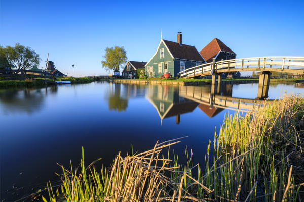 Wood houses and windmill  are reflected in the blue water of river Zaan Zaanse Schans North Holland The Netherlands Europe