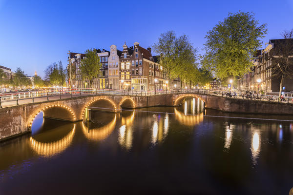 Dusk lights on the typical buildings and bridges reflected in a typical canal Amsterdam Holland The Netherlands Europe